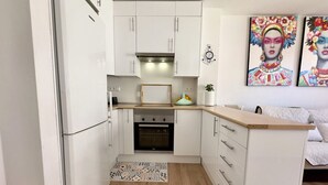 Eine kompakte Küche mit weißen Schränken, einer Mikrowelle und einem Backofen. Auf dem Boden liegt ein kleiner Teppich und auf der Arbeitsfläche steht eine Pflanze.