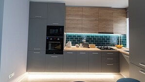 A modern kitchen with grey cabinets, a wooden accent wall, and a blue-tiled backsplash.