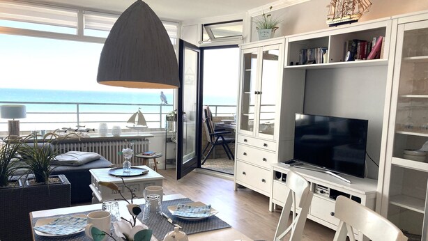 A modern living room with a large TV, white cabinets, and a view of the ocean.