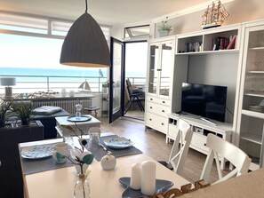 Una sala de estar moderna con un televisor grande, armarios blancos y vista al océano.