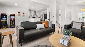 A modern living room with a dark leather sofa, a coffee table, and arcade games. - 5BR Luxury Oasis w/ Pool & Spa + Games and MORE! (North Las Vegas)