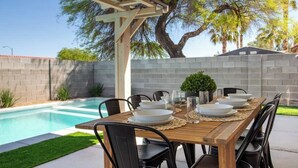A wooden dining table set for six with plates, glasses, and a centerpiece. - 5BR Luxury Oasis w/ Pool & Spa + Games and MORE! (North Las Vegas)