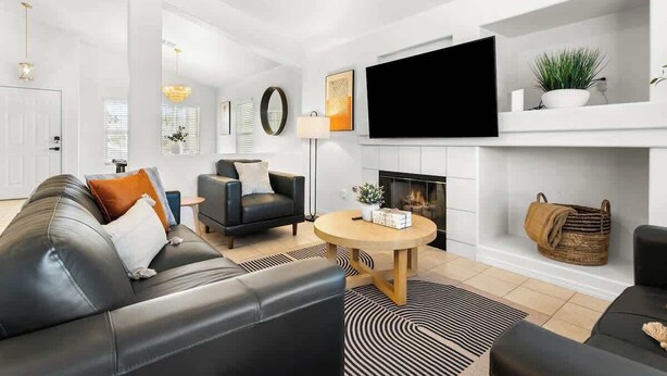 A modern living room with a black leather sofa, a round wooden coffee table, and a flat-screen TV mounted on the wall. - 5BR Luxury Oasis w/ Pool & Spa + Games and MORE! (North Las Vegas)
