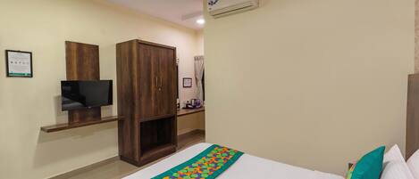 A hotel room with a bed, a TV, a wardrobe, and an air conditioning unit.