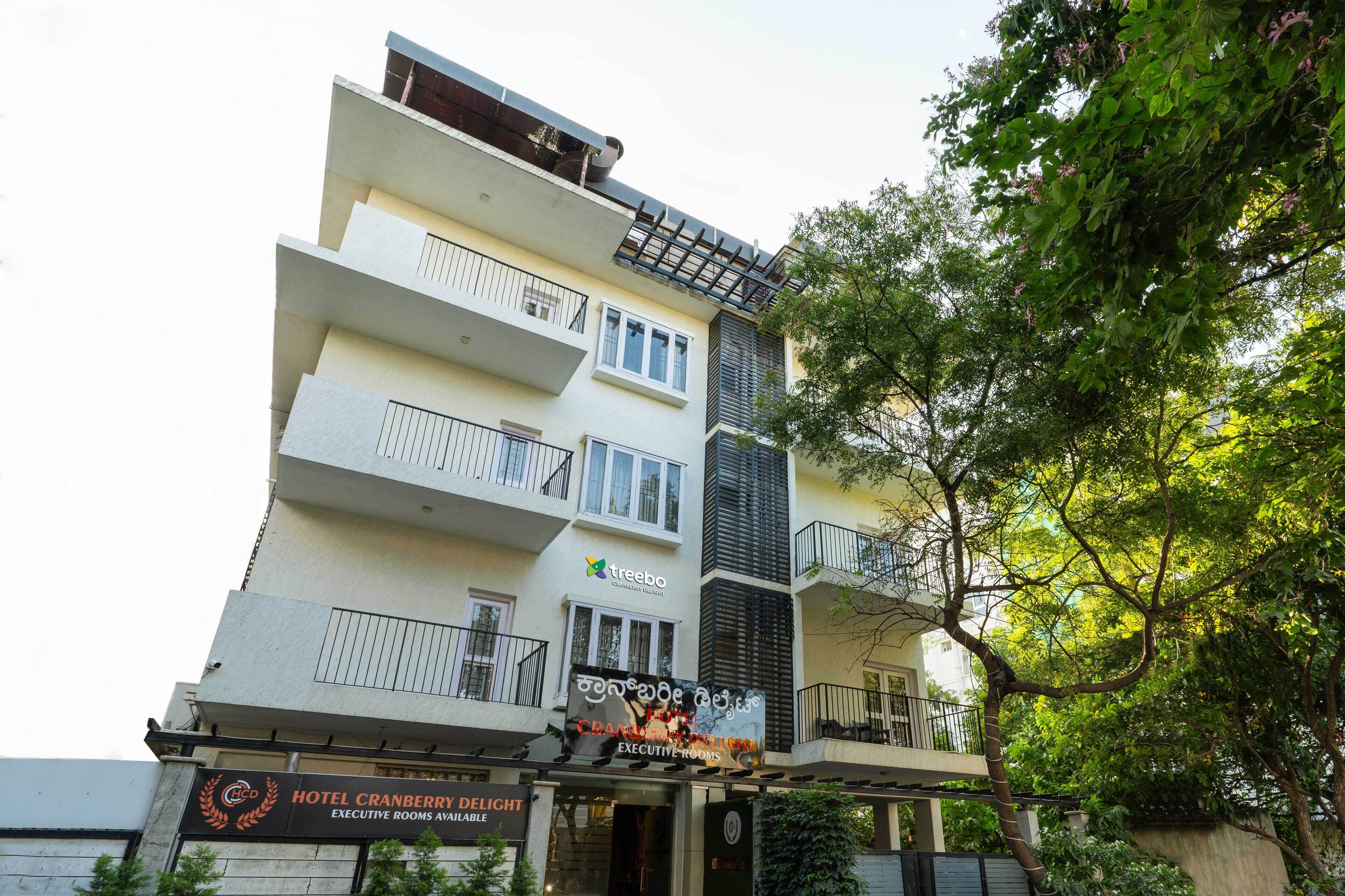 Ένα πολυώροφο ξενοδοχείο με μπαλκόνια, μια πινακίδα με την ένδειξη «Hotel Cranberry Delight» και μια πινακίδα «Treebo», η οπ οία υποδεικνύει ένα κοντινό εστιατόριο.