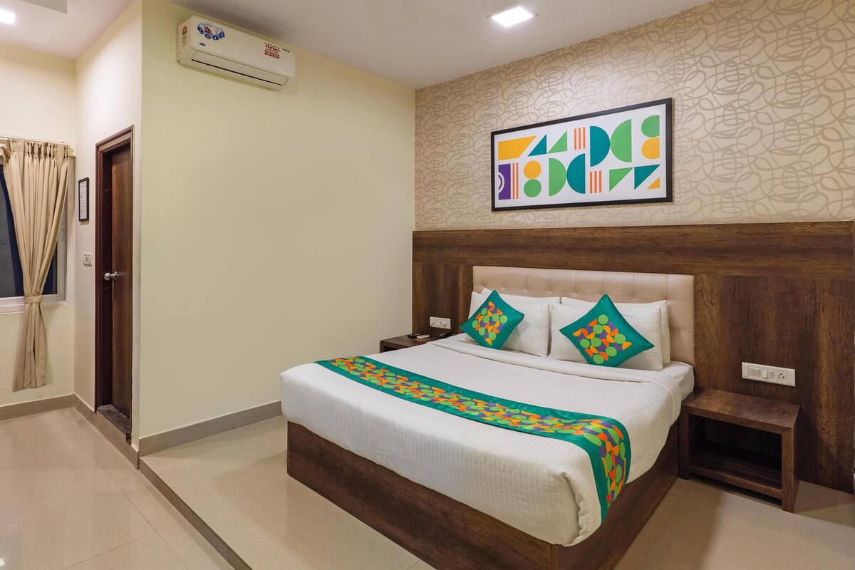 Habitación de hotel con una cama grande, cabecero de madera, aire acondicionado fijado a la pared y una obra de arte abstracta enmarcada sobre la cama.