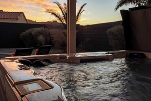 A hot tub with a view of a sunset, palm trees, and a brick wall.