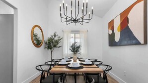 Ein Esszimmer mit einem Holztisch, gedeckt für sechs Personen, umgeben von schwarzen Stühlen. Eine Chandelier hängt von der Decke, und ein Gemälde ist an der Wand.