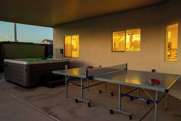 A ping pong table with a table tennis ball and paddle, a pool table with a green felt surface, and a sofa.