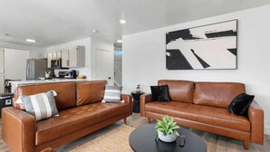Ein modernes Wohnzimmer mit zwei braunen Ledersofas, einem runden Couchtisch und einem minimalistischen Schwarz-Weiß-Kunstwerk an der Wand.