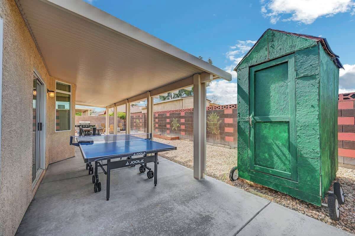 A covered outdoor area with a ping pong table, a green shed, and a brick wall.