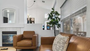 Una sala de estar moderna con un sofá de cuero marrón, un sillón a juego y una mesa redonda de centro. Se ve un espejo grande y una chimenea al fondo.