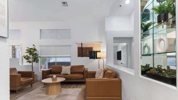 Una sala de estar moderna con un sofá de cuero marrón, una mesa de centro de madera y un estante de vidrio con plantas.