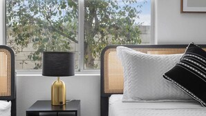 Un dormitorio con cama, mesita de noche, lámpara y ventana con vistas a árboles.