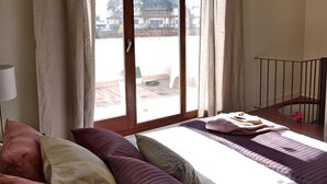 Ein Schlafzimmer mit einer großen Glasschiebetür, einem Bett mit vielen Kissen, einem Nachttisch und Blick auf ein Gebäude.