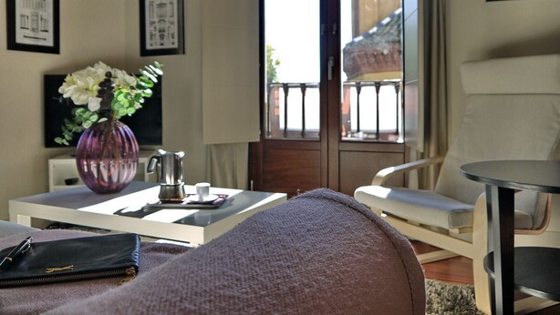Ein modernes Wohnzimmer mit einer Couch, einem Couchtisch mit Blumenvase, einem Sessel und Blick auf ein Gebäude durch eine Glastür.