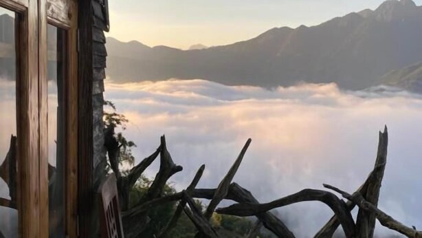 A rustic cabin with a wooden bench and a view of a mountain range and clouds below. - Sapa Mackeno (Sa Pa)
