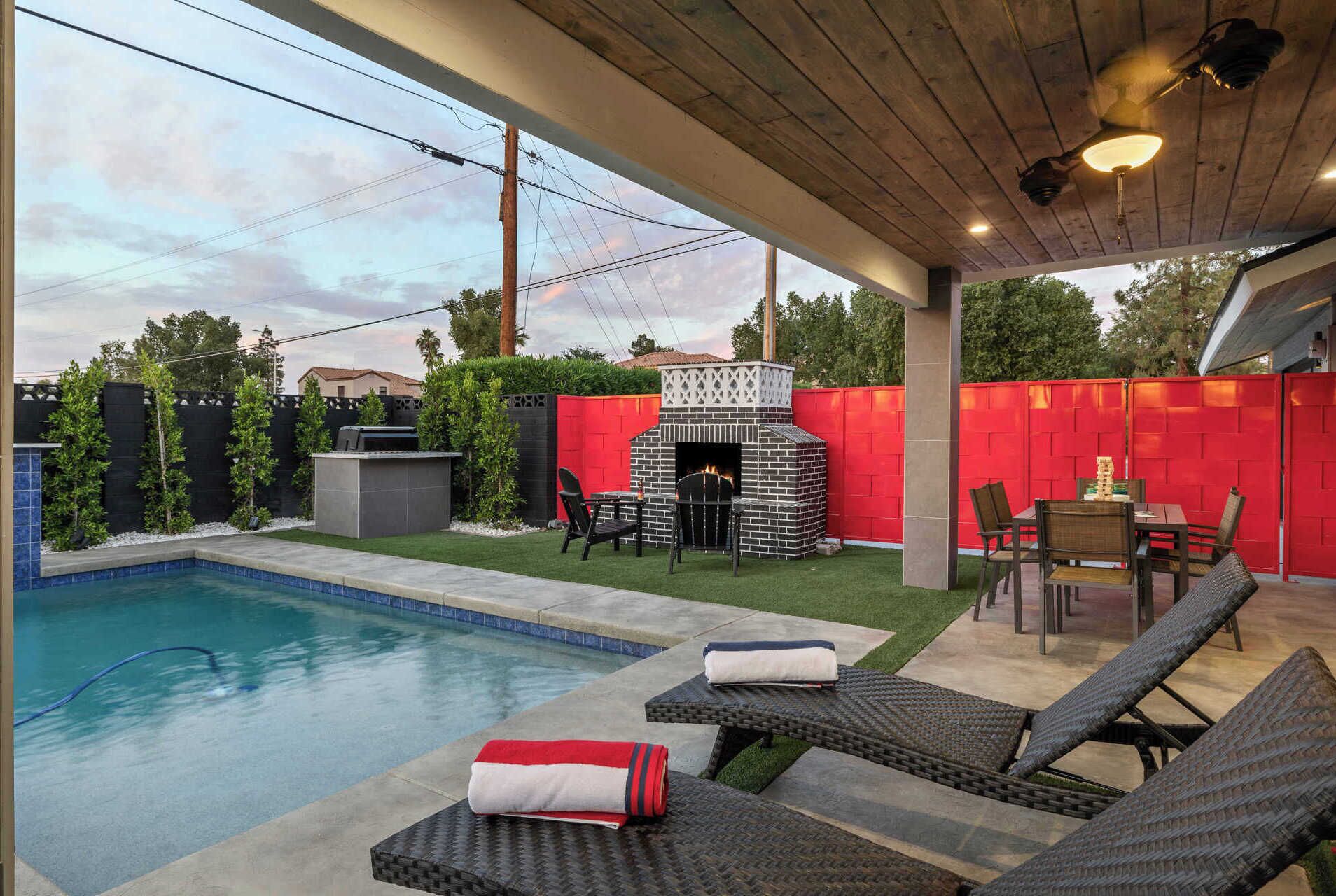 A backyard with a swimming pool, a brick outdoor fireplace, and lounge chairs.