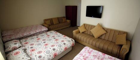 A room with three beds, two sofas, and a TV on the wall.