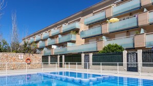 Una piscina con solárium de baldosas, rodeada por un muro de piedra y una valla de metal.