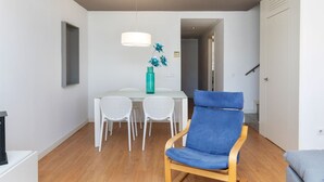 Una sala de estar moderna con comedor, que incluye un sillón azul, una mesa de comedor blanca y un florero azul verdoso con flores azules.