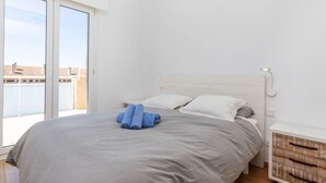 Un dormitorio con una cama grande, una mesita de noche y vistas a la ciudad a través de una puerta corredera.