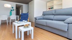 Una sala moderna con un sofá gris, una mesita de centro blanca y un sillón azul.