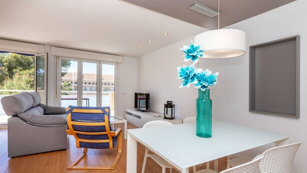 Una sala moderna con un sofá, un sillón a rayas, una mesa blanca y un jarrón azul turquesa con flores azules.