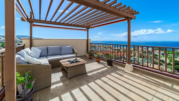 Un espace extérieur aménagé, abrité et doté d’un canapé et d’une table basse, de plantes en pot, et offrant une vue sur la mer.