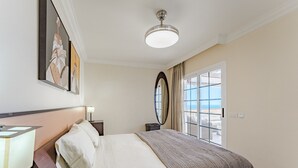 Une chambre d’hôtel avec un lit, une table de chevet, une lampe, une fenêtre avec des rideaux et un ventilateur de plafond.
