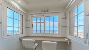 Une petite salle de bain d’angle avec deux tabourets de bar blancs, une fenêtre ornée d’un panneau indiquant le mot « PAIX », et une vue sur la ville.
