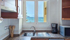A kitchen with a view of the sea, a sink, a coffee maker, and wooden cabinets. - GRAN SOL sea front apartment (Calpe)