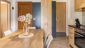 A modern kitchen with wooden cabinets, a dining table with chairs, and a vase of flowers. - Miki Mhouse by Interhome (Lago di Mezzola)