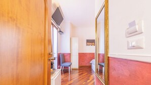 A hotel room with a wooden door, a bed, a TV mounted on the wall, and a large mirror. - Room-camera Doppia in History House (Rome)