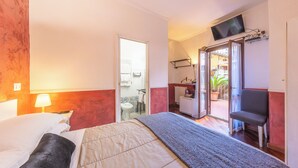 A hotel room with a bed, a chair, a TV, and a bathroom visible through an open door. - Room-camera Doppia in History House (Rome)