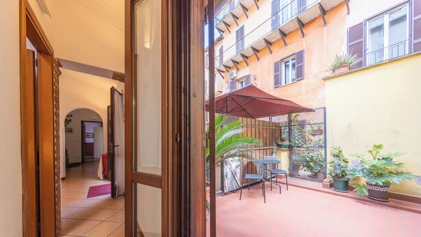 An open door leading to a courtyard with a tiled floor, a red umbrella, and potted plants. - Room-camera Doppia in History House (Rome)