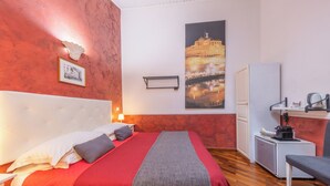 A hotel room with a large bed, a desk with a chair, a small kitchenette, and a large framed picture on the wall. - Room-skylight Double Room in History Hou (Rome)