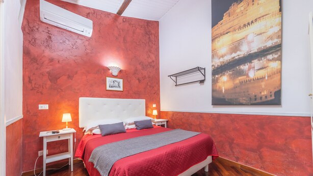 A bedroom with a red wall, a large bed with a white headboard, two bedside tables with lamps, and a framed picture above the bed. - Room-skylight Double Room in History Hou (Rome)