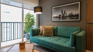 A teal sofa with two cushions, a cityscape framed picture, a hanging lamp, and a potted plant. - w * | Marvelous 1BR in the Heart of Barranco (Lima)