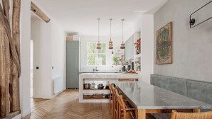 Moderni keittiö, jossa on kalanruotokuviollinen puulattia, keskellä oleva saareke istuimineen, riippuvalaisimet ja näkymä ulos.