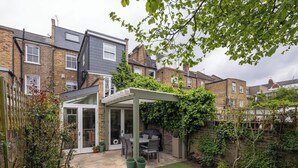 Un jardin à l’arrière d’une maison d’habitation, comprenant une terrasse, un espace salon abrité et une pelouse.