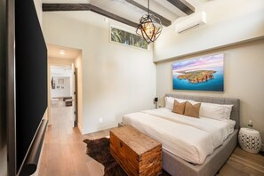 Ein Schlafzimmer mit einem großen Bett, einer Holzkiste, einem Landschaftsbild und einem Flur, der in einen anderen Raum führt.