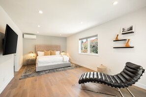 A bedroom with a bed, bedside tables, a TV, a window, and a chair.