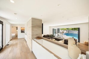 A modern kitchen with a built-in island, a seating area with a pool view, and a wooden floor.