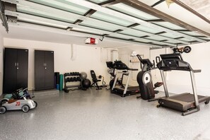 Ein Fitnessraum mit Trainingsgeräten, Laufband, Gewichten und einem Spielzeug-Fahrzeug für Kinder.