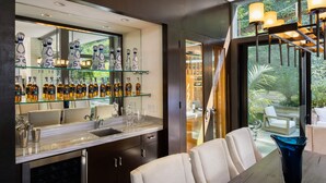 A modern kitchen with a large island, glass shelves with bottles, and a view of the outdoors. - Villa Aman by Stay Awhile Villas (Beverly Hills)