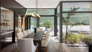 A modern dining area with a long table, white chairs, and a hanging light fixture. - Villa Aman by Stay Awhile Villas (Beverly Hills)