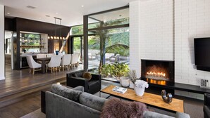 A modern living room with a fireplace, a television, and a dining area with a bar. - Villa Aman by Stay Awhile Villas (Beverly Hills)