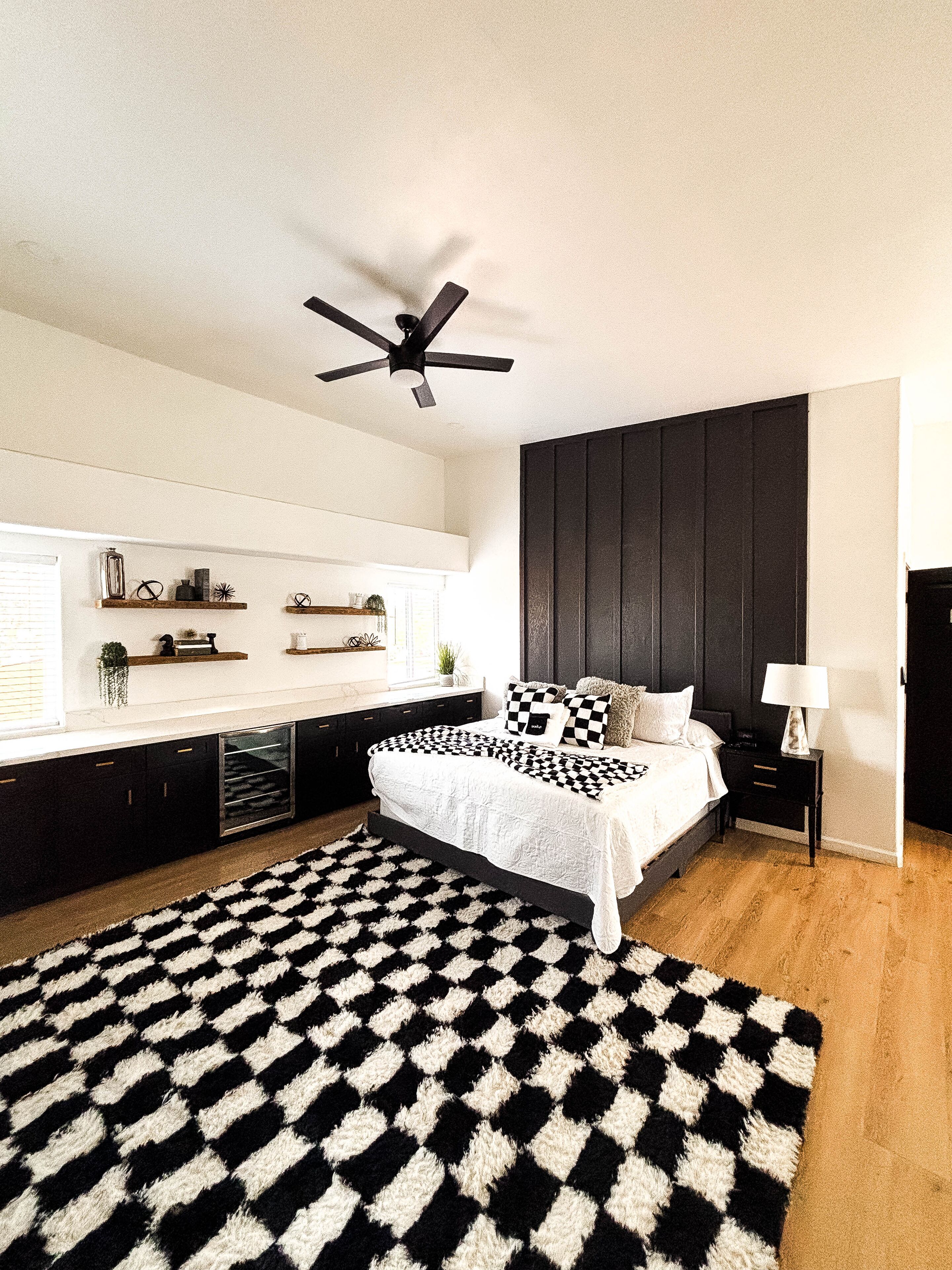 A modern bedroom with a bed, a ceiling fan, a black and white rug, and built-in shelves.