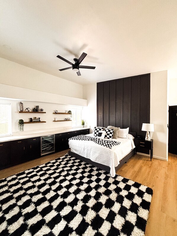 A modern bedroom with a bed, a ceiling fan, a black and white rug, and built-in shelves.